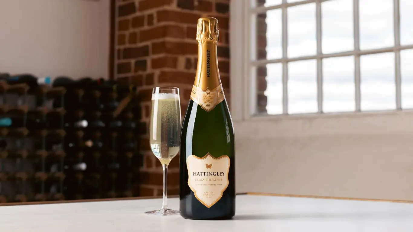 Bottle of English sparkling wine next to a glass of English sparkling wine on a table in front of a window